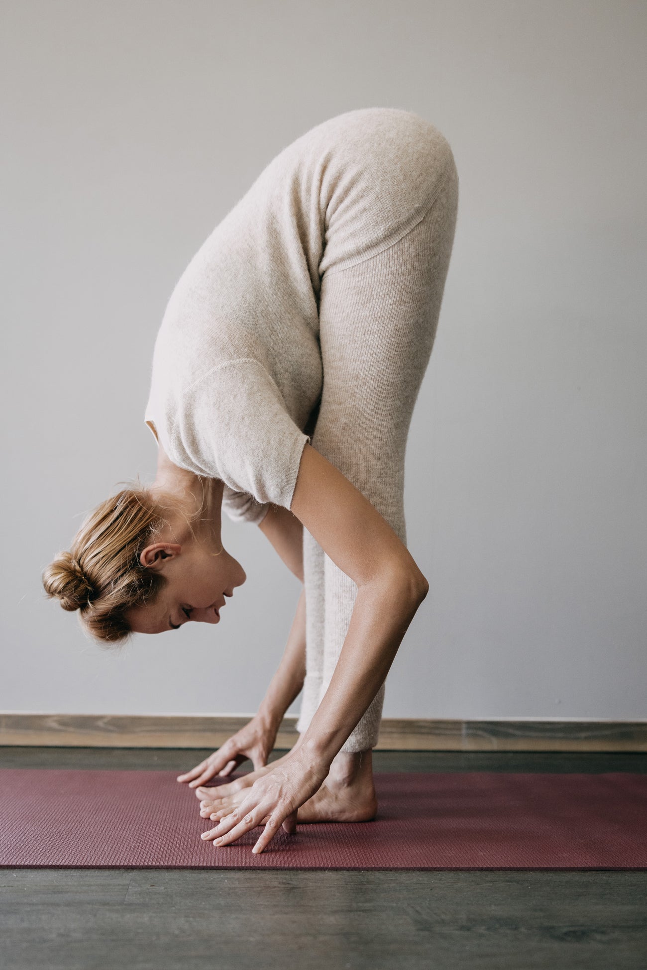 Frau in beige ALPAKA Damen Leggins ALBERTA auf roter Yogamatte, zeigt stehende Vorwärtsbeuge. Perfekt für gemütliche Wärme und Komfort.