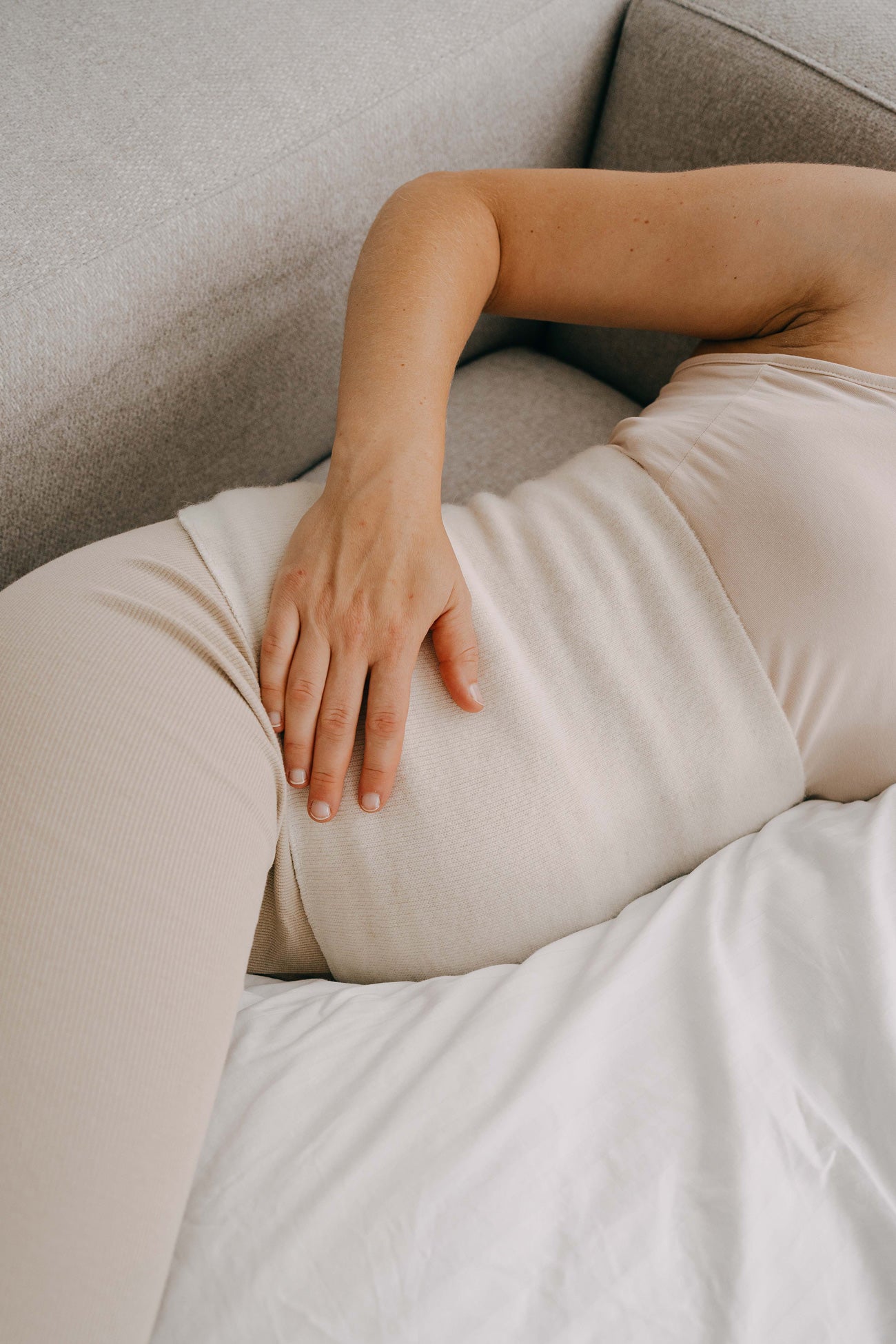 Person auf grauem Sofa in cremefarbenem, geripptem Set, trägt ALPAKA Rückenwärmer ALVA für entspannende Wärme und Komfort, ideal für empfindliche Haut.