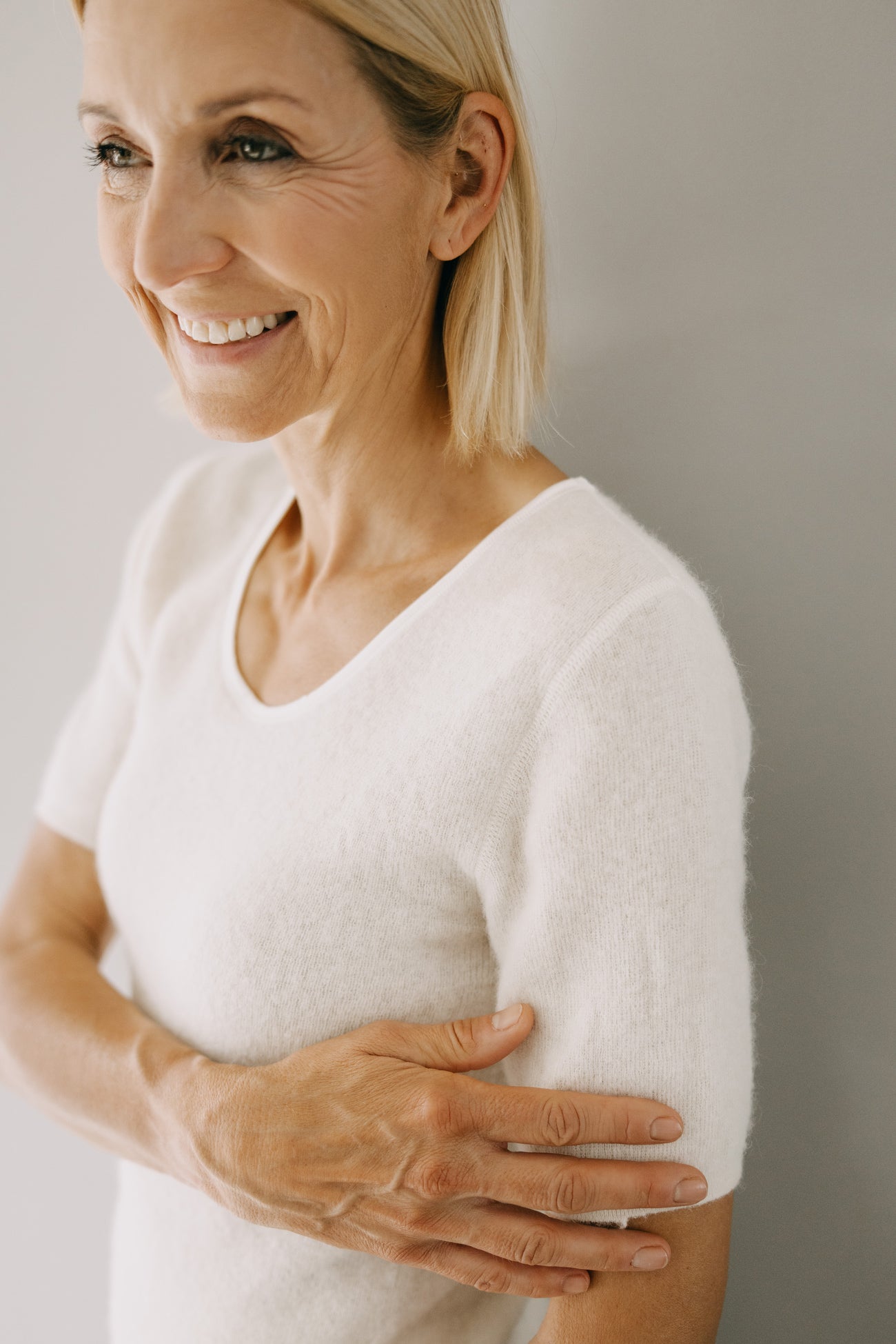 Frau in weichem, weißen ALPAKA Damen Shirt AMALYA, lächelt sanft. Das Shirt bietet Komfort durch Alpakafaser, wärmt und hält die Haut trocken.
