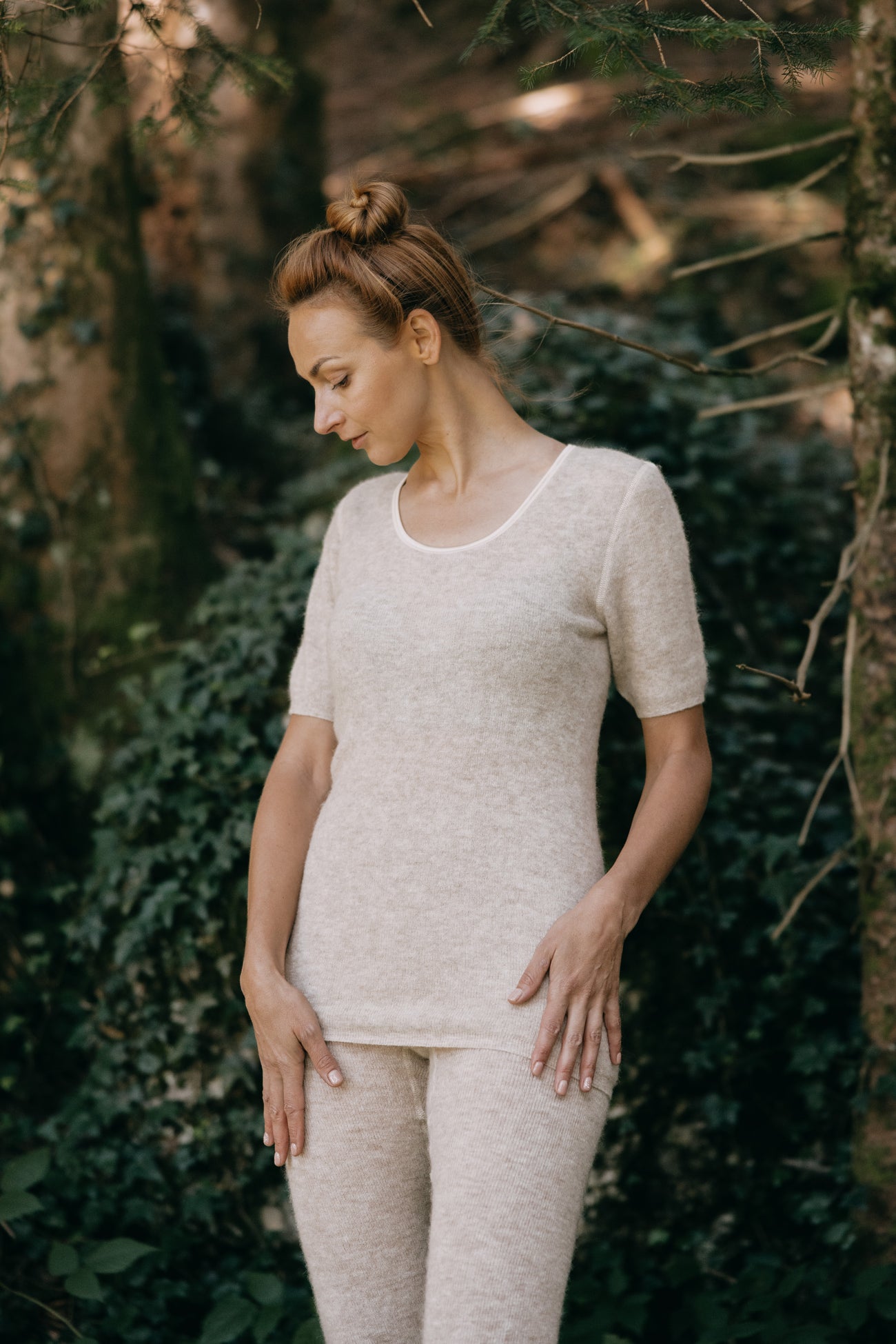 Frau im Wald trägt das ALPAKA Damen Shirt AMALYA: beigefarbenes, kurzärmeliges, nahtloses Oberteil mit angenehmem Tragekomfort, ideal für wechselnde Temperaturen.