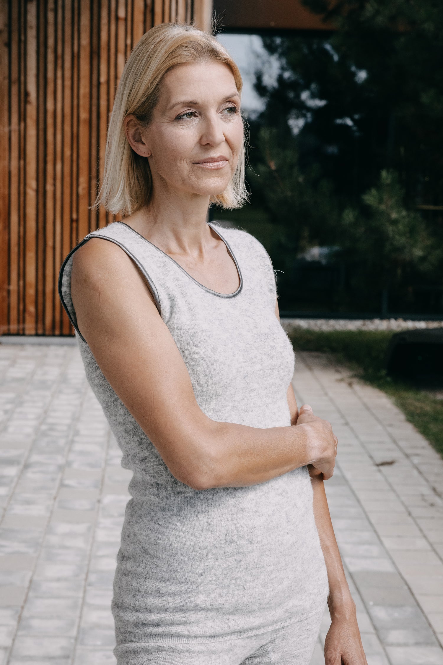 Frau trägt das ärmellose ALPAKA Damen Top AYDA, gestrickt ohne Nähte, ideal für kühle Temperaturen dank wärmespeichernder Alpakafaser, auf einer Terrasse stehend.