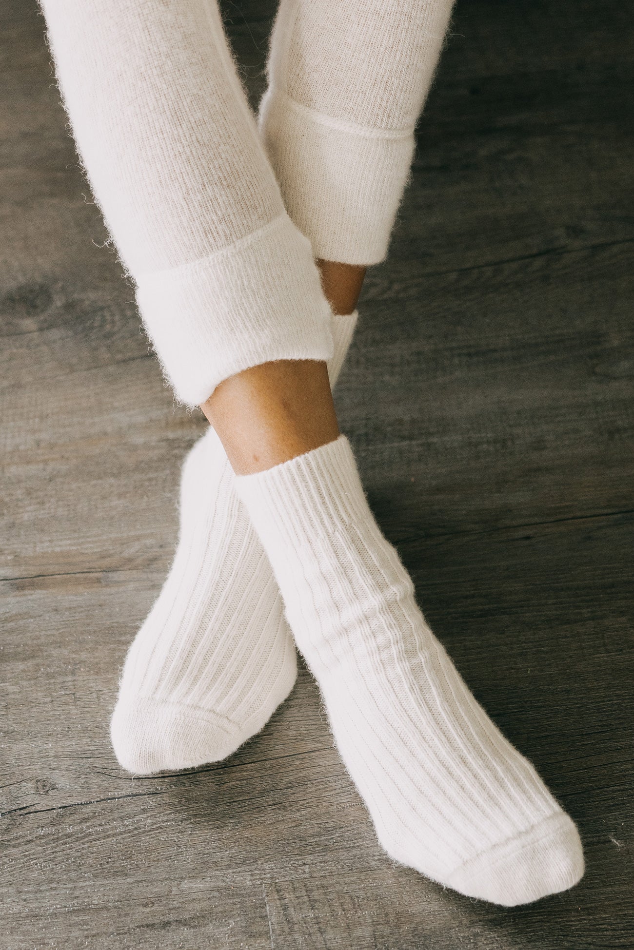 Nahaufnahme von Füßen in weißen, gerippten ALPAKA Kuschelsocken ALMA auf Holzfußboden, betont durch Komfort und Wärmespeicherung der Alpakafasern.