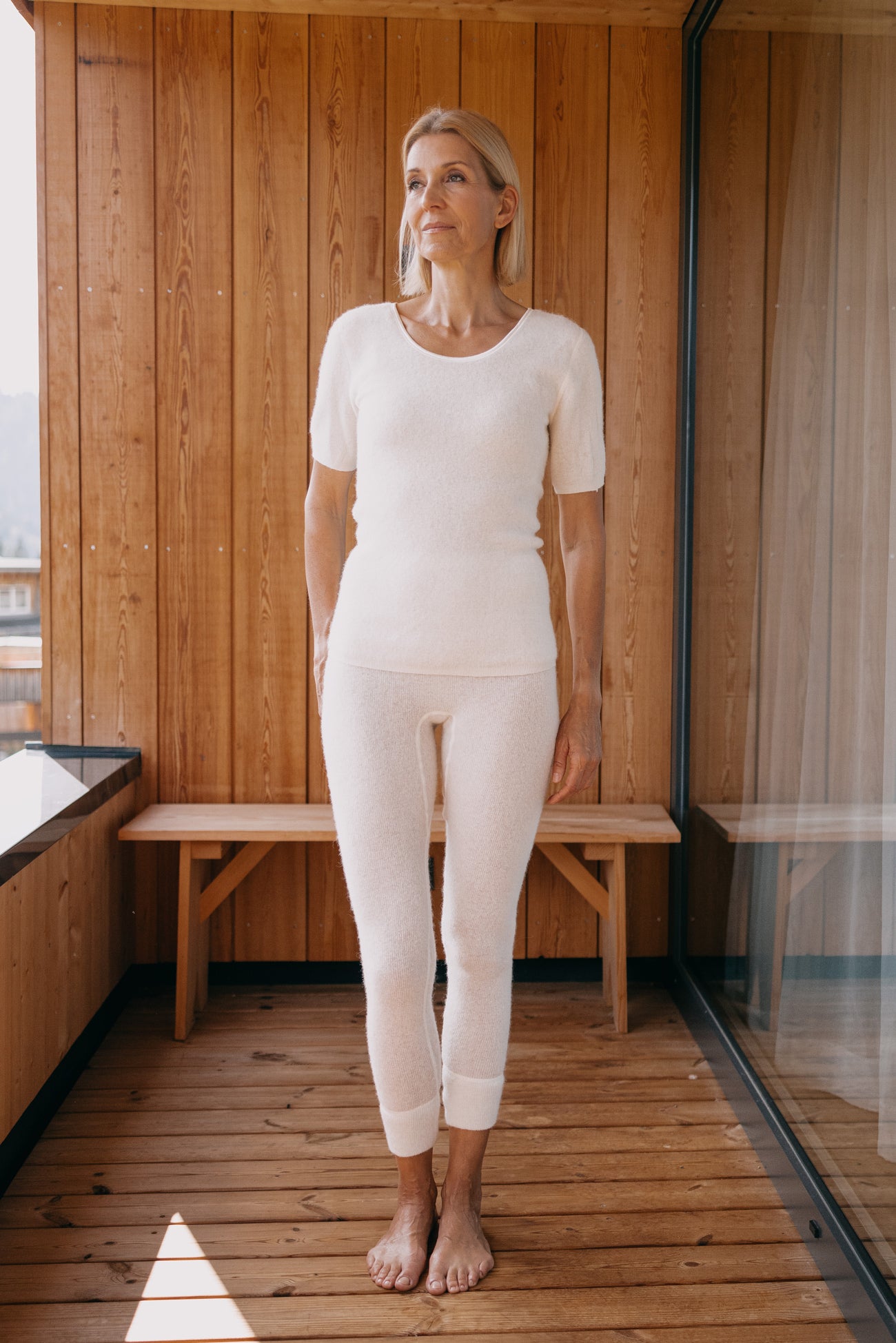 Frau in ALPAKA Damen Leggins ALBERTA aus weichem, weißem Strick auf Holzterrasse. Ideal für Wärme und Komfort durch einzigartige Thermoeigenschaften der Alpakafaser.