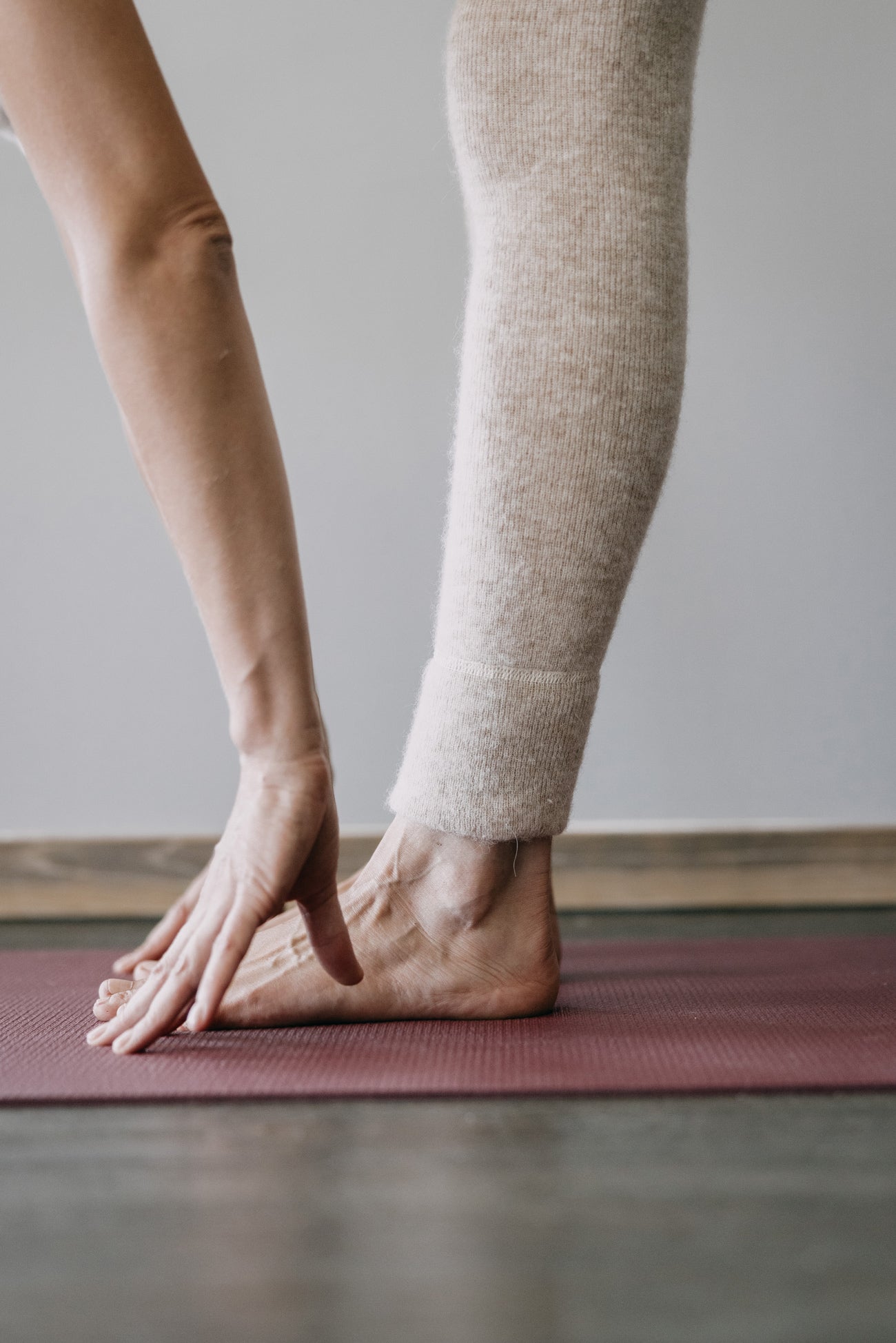Person macht Vorwärtsbeuge auf roter Matte, trägt ALPAKA Damen Leggings ALBERTA aus Alpakafaser, sichtbar ist ein Fuß und ein flauschiger, warmer Hosenbein.