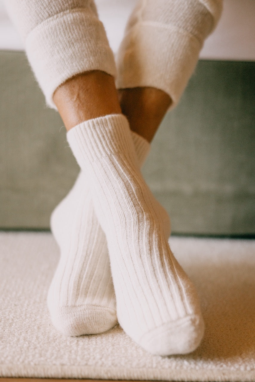 ALPAKA Kuschelsocken ALMA an Füßen auf Teppichboden, bieten durch Alpakafasern wohltuende Wärme und Komfort, ideal für empfindliche Haut und stilvolle Gemütlichkeit.